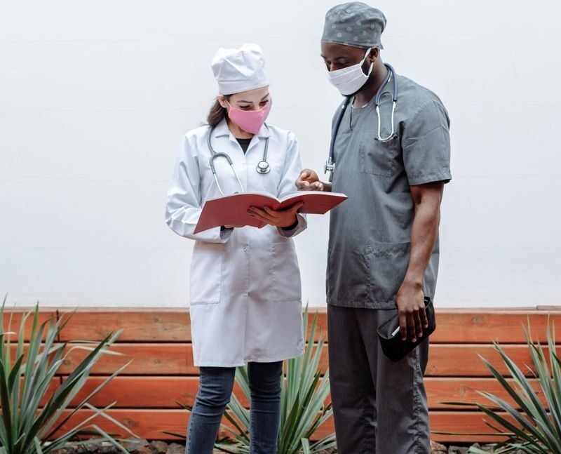 Medical professionals in face masks reviewing documents outdoors, promoting safety during pandemic.